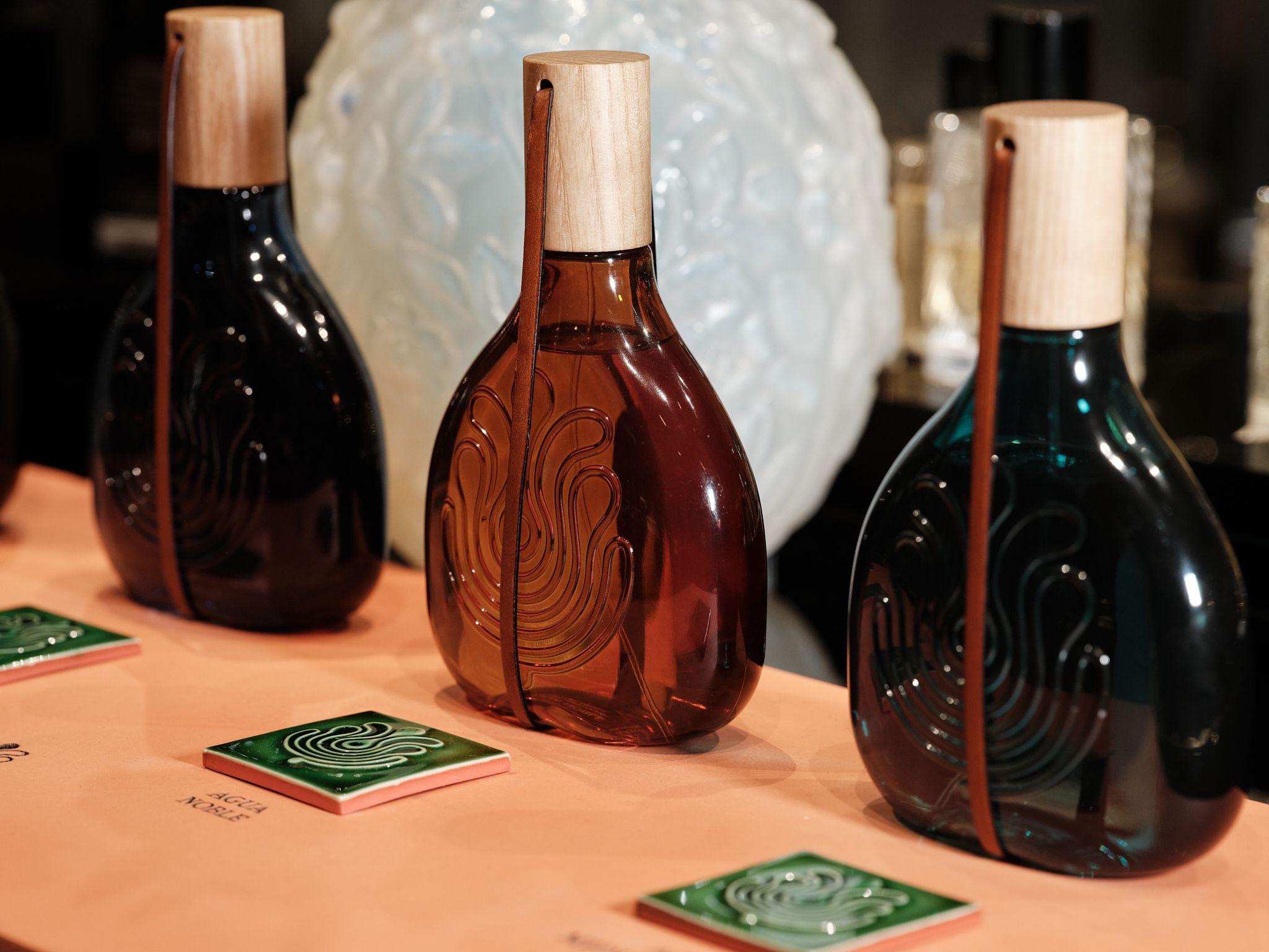 Three Colonias Absolutas Puig fragrance bottles displayed on a counter beside a vase of white roses